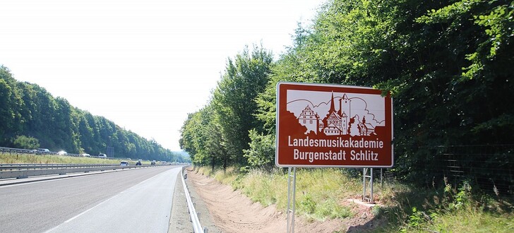 Zwei Hinweisschilder auf der A 7 Richtung Süden nach der Raststätte Großenmoor und Richtung Norden kurz vor der Anschlussstelle Hünfeld/Schlitz werben für die Landesmusikakademie und die Stadt Schlitz selbst